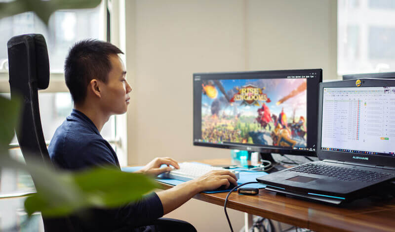 Official Rise of Kingdoms website photo showing a player at a desk with the game running on a desktop monitor